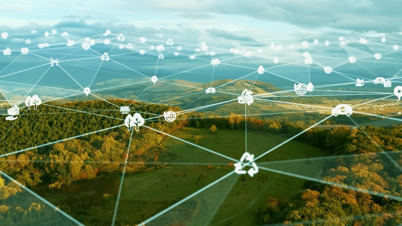 Aerial view of a forested valley overlaid with a glowing network of connected icons, from the Communications of the ACM cover feature on the Internet of Batteryless Things.